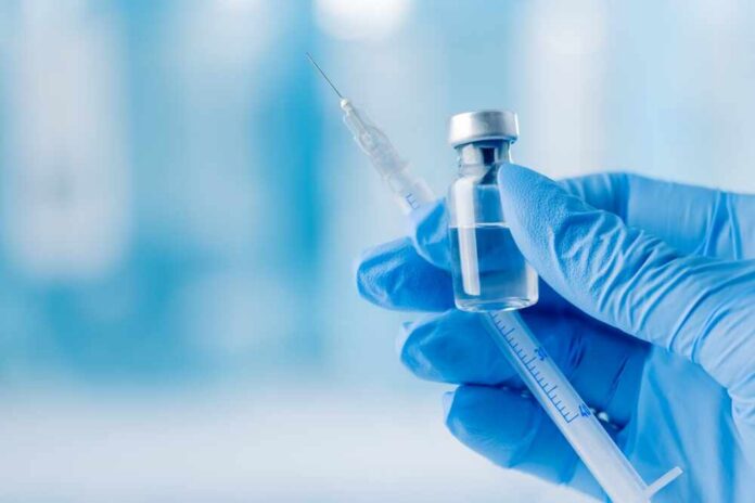 A gloved hand holding a syringe and a vial of liquid