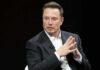 Musk Money Tsunami Hits Midterms Man in suit, hands clasped, black background.