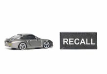 Seat Belts Fail? Massive Recall A miniature gray sports car next to a black sign that reads 'RECALL'