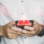 Hands holding a smartphone with warning icons overlay