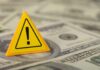 $4 Returns — Consumer Confidence Craters A yellow warning sign placed on a pile of dollar bills