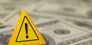 A yellow warning sign placed on a pile of dollar bills