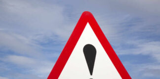 Warning road sign with exclamation mark against a cloudy sky