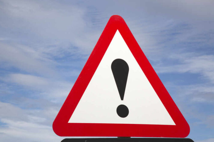 Warning road sign with exclamation mark against a cloudy sky