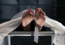 Feet of a covered body on a morgue table with a toe tag