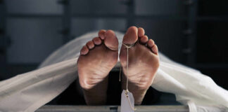 Feet of a covered body on a morgue table with a toe tag