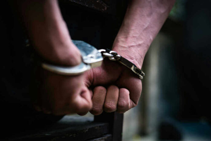 shutterstock_1338116366 Close-up of hands in handcuffs behind back.