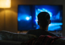 Person sitting on a couch watching a television screen in a dimly lit room