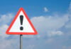 Blast Paralyzes Train Station – Terrorism? Triangle warning sign with exclamation mark against sky.