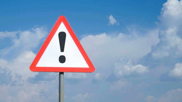 shutterstock_1783779719 Triangle warning sign with exclamation mark against sky.