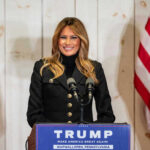 Woman speaking at Trump podium, two American flags present.