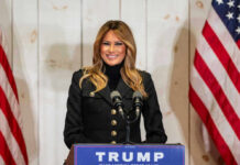 Woman speaking at Trump podium, two American flags present.