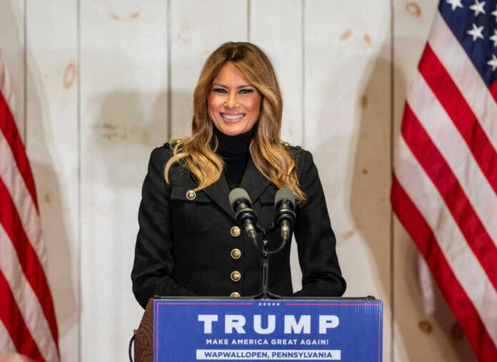 shutterstock_1844845672 Woman speaking at Trump podium, two American flags present.