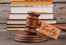 A wooden gavel with a tag reading 'Guilty' next to stacked books