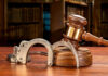Courthouse Chaos: Defense Lawyer ARRESTED Wooden gavel and handcuffs on a table.