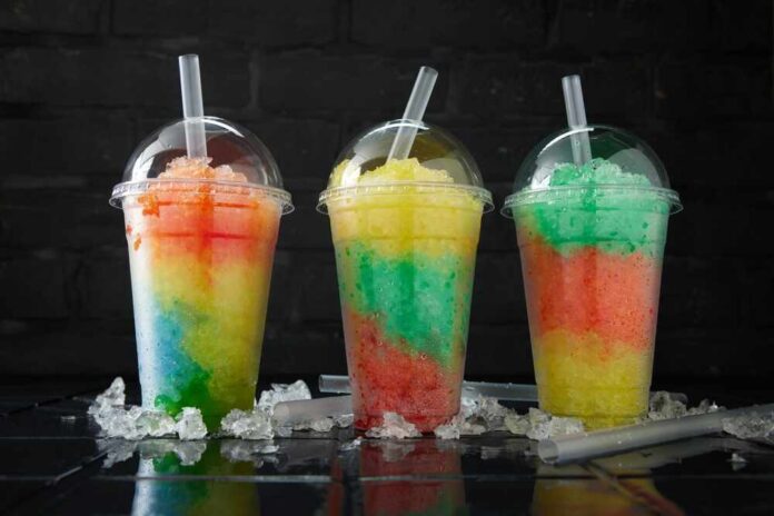 Three colorful shaved ice drinks in clear plastic cups with domed lids