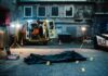 Police investigation at a crime scene with a covered body and evidence markers