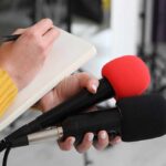 Dirty Soda Outsells Utah — What’s Going On? Journalist holding two microphones while writing in a notebook