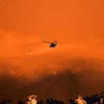 Massive Resort Inferno: Arson Suspicions Explode Helicopter flies over a wildfire at sunset with smoke and embers in the sky