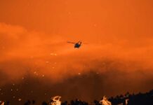 Massive Resort Inferno: Arson Suspicions Explode Helicopter flies over a wildfire at sunset with smoke and embers in the sky