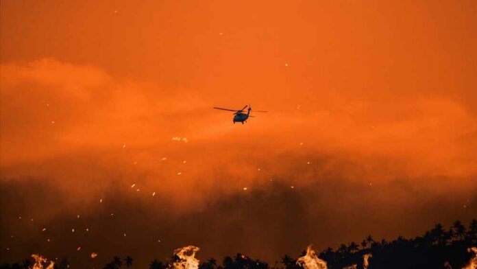 Firefighting,Helicopter,Battles,Flames,In,Los,Angeles,During,Wildfires,Of Helicopter flies over a wildfire at sunset with smoke and embers in the sky