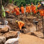 Rescue workers in orange uniforms search a landslide site with a dog