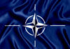 NATO’s Brutal Plan for Adversary NATO flag with white compass emblem on blue background.