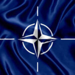 NATO flag with white compass emblem on blue background.