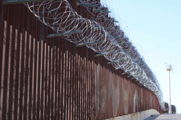 Large,Loops,Of,Sharp,Razor,Wire,Hang,On,Bollard,Style Border fence topped with coils of razor wire