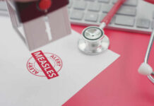 Statewide Alarm Over Measles – What’s Coming? A stamp marking 'MEASLES ALERT' on a piece of paper next to a stethoscope and keyboard