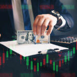 Businessperson holding a hundred-dollar bill over documents with stock chart overlay