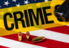 A gun and bullets on an American flag with a crime scene marker