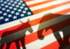 Shock: Republican Backs Democrat Donkey and elephant shadows on American flag background.