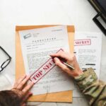 A person in military attire marking a classified document with a red 'FOR SECRET' stamp